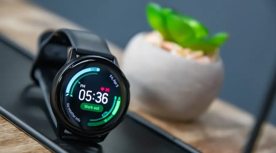 اسمارت واچ Samsung Galaxy Watch Active مشکی صفحه گرد با نمایش ساعت و ضربان قلب بر روی میز مشکی کنار گلدان سفید