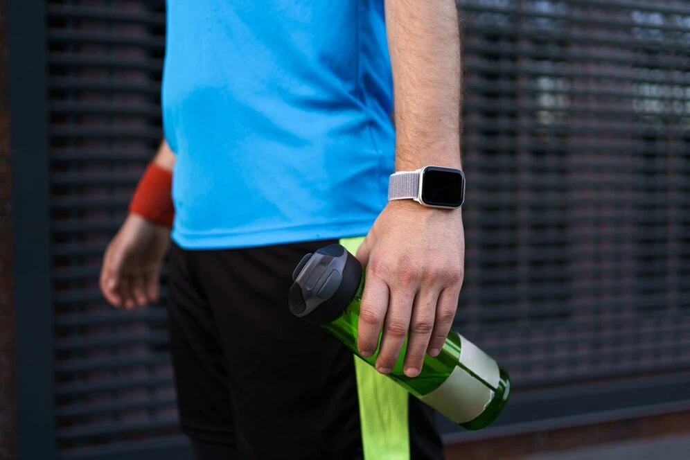 ساعت هوشمند ورزشی در دست یک مرد ورزشکار همراه با قمقمه